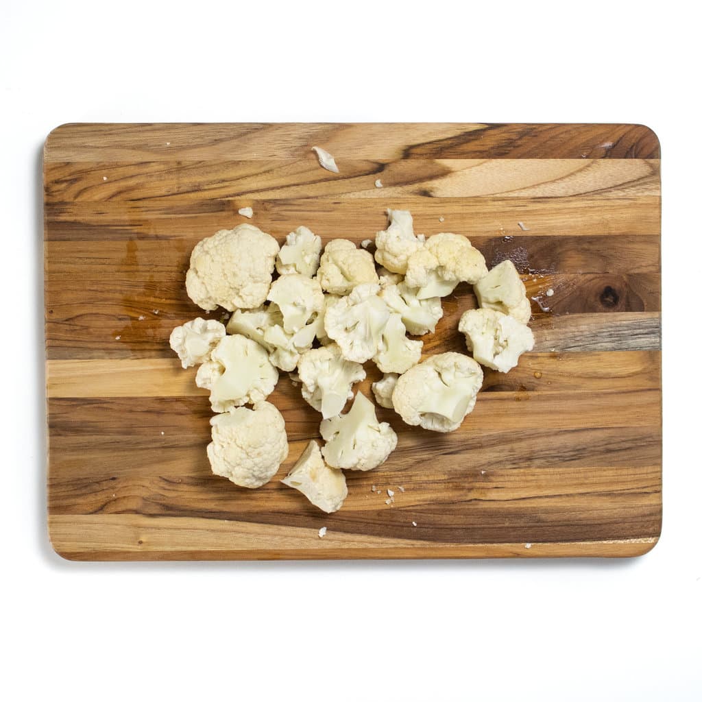 A wooden cutting board with a bunch of cauliflower florets.