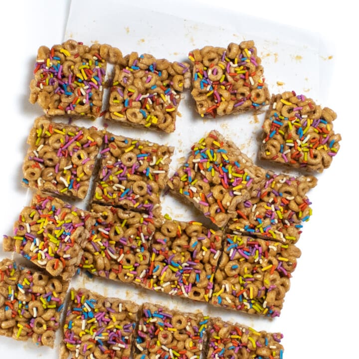A batch of cereal bars with colorful sprinkles sitting on parchment paper against a white background.