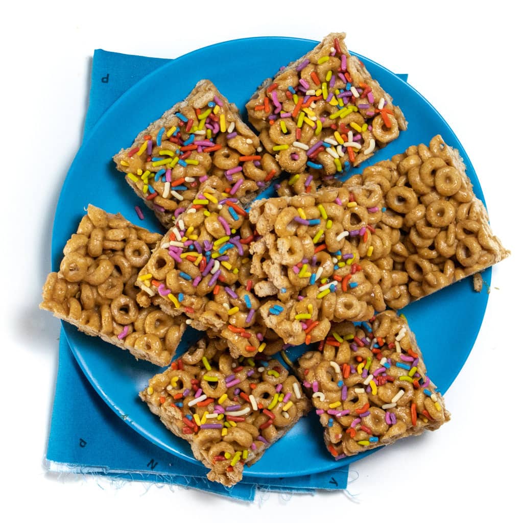 A plate of healthy cereal bars cut into squares with a blue kids napkin against a white background.
