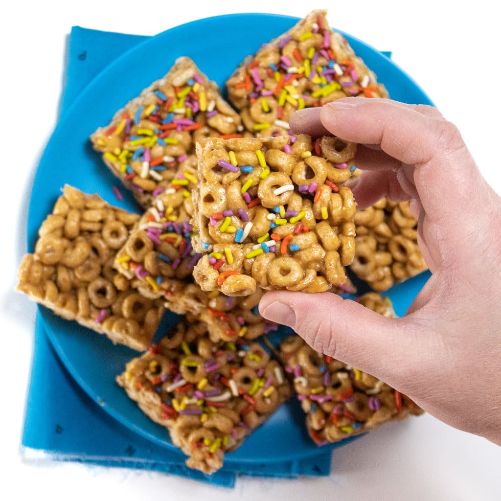A hand holding up a cereal bar against a plate full of cereal bars.
