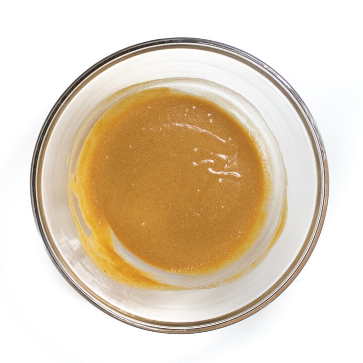 Clear glass bowl against a white backdrop with mixed peanut butter and agave nectar.