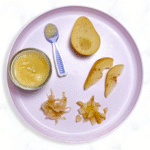 purple baby plate sitting on a white marble counter, with different ways to serve pear to your baby - purees, cooked wedges and slices all with cinnamon.