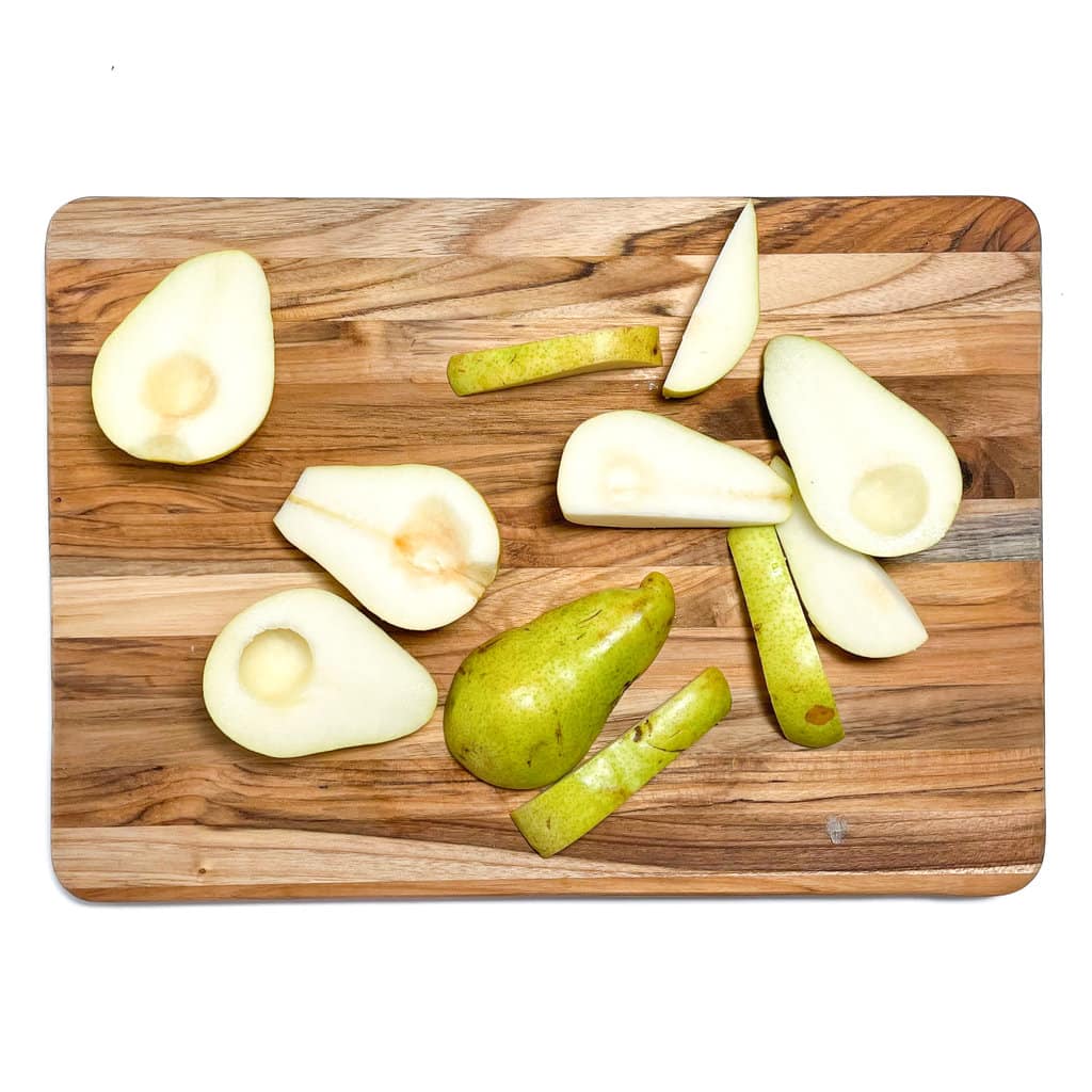 A wooden cutting board against a white background with chopped pears on top.