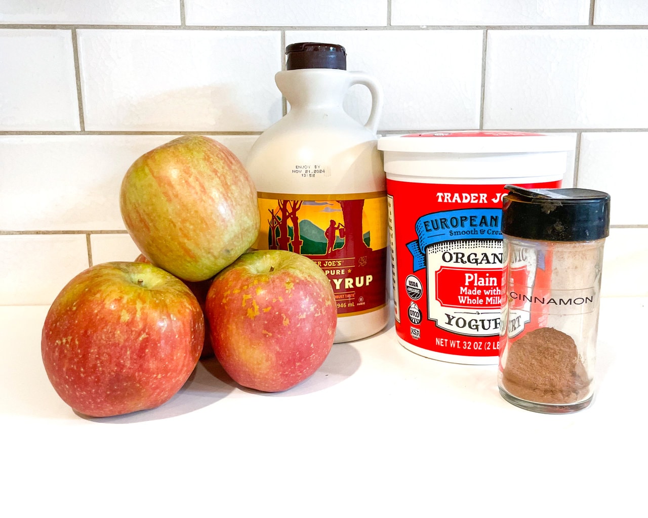 A kitchen counter with ingredients for apple yogurt – apples, maple syrup, yogurt, cinnamon.
