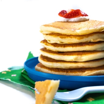 Side view of a stack of yogurt pancakes with yogurt and strawberries on top sitting on a blue kids plate.