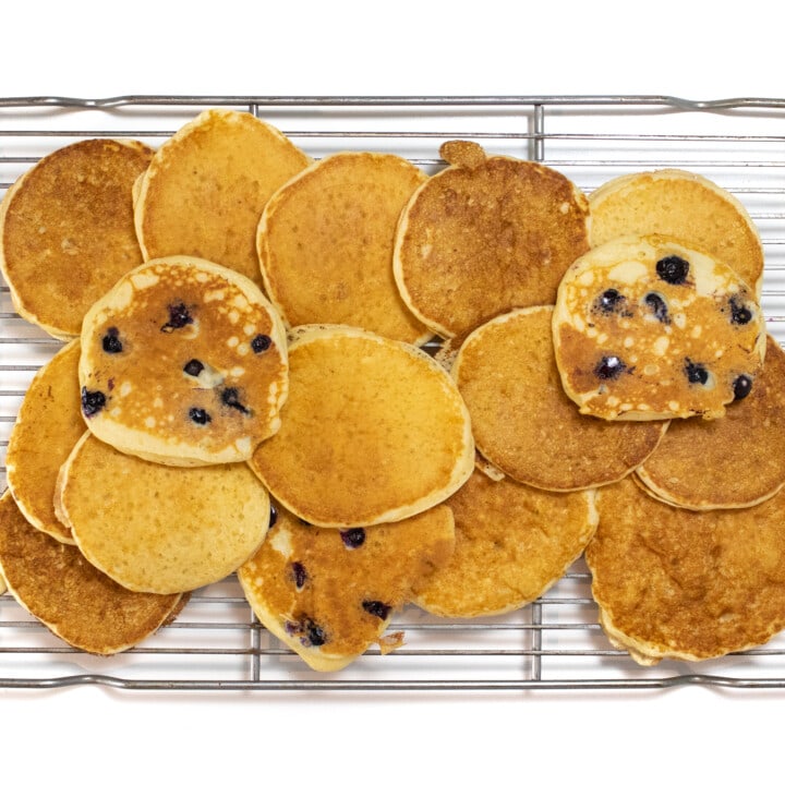 A cooling rack against a white background on top of the cooling rack are yogurt pancakes some with blueberries.