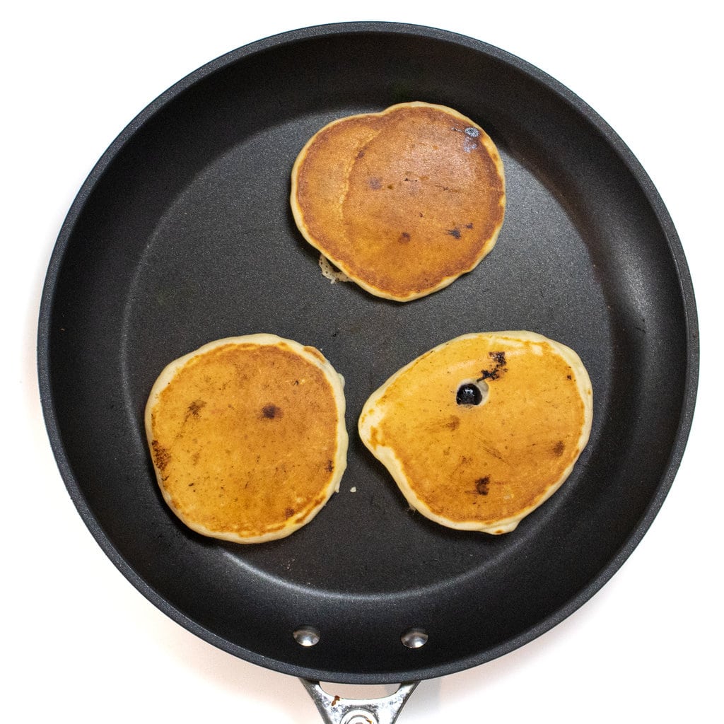 A skillet with three yogurt pancakes being cooked.