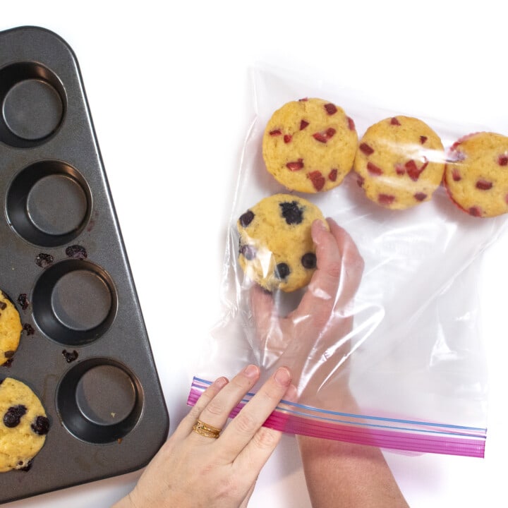 Two hands putting fresh muffins into a Ziploc bag ready to be frozen.