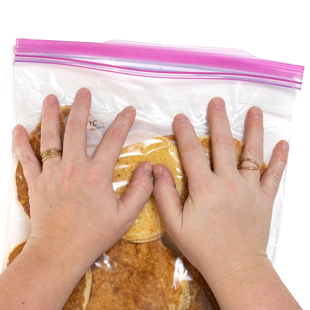 Two hands pressing down on a Ziploc bag full of pancakes.