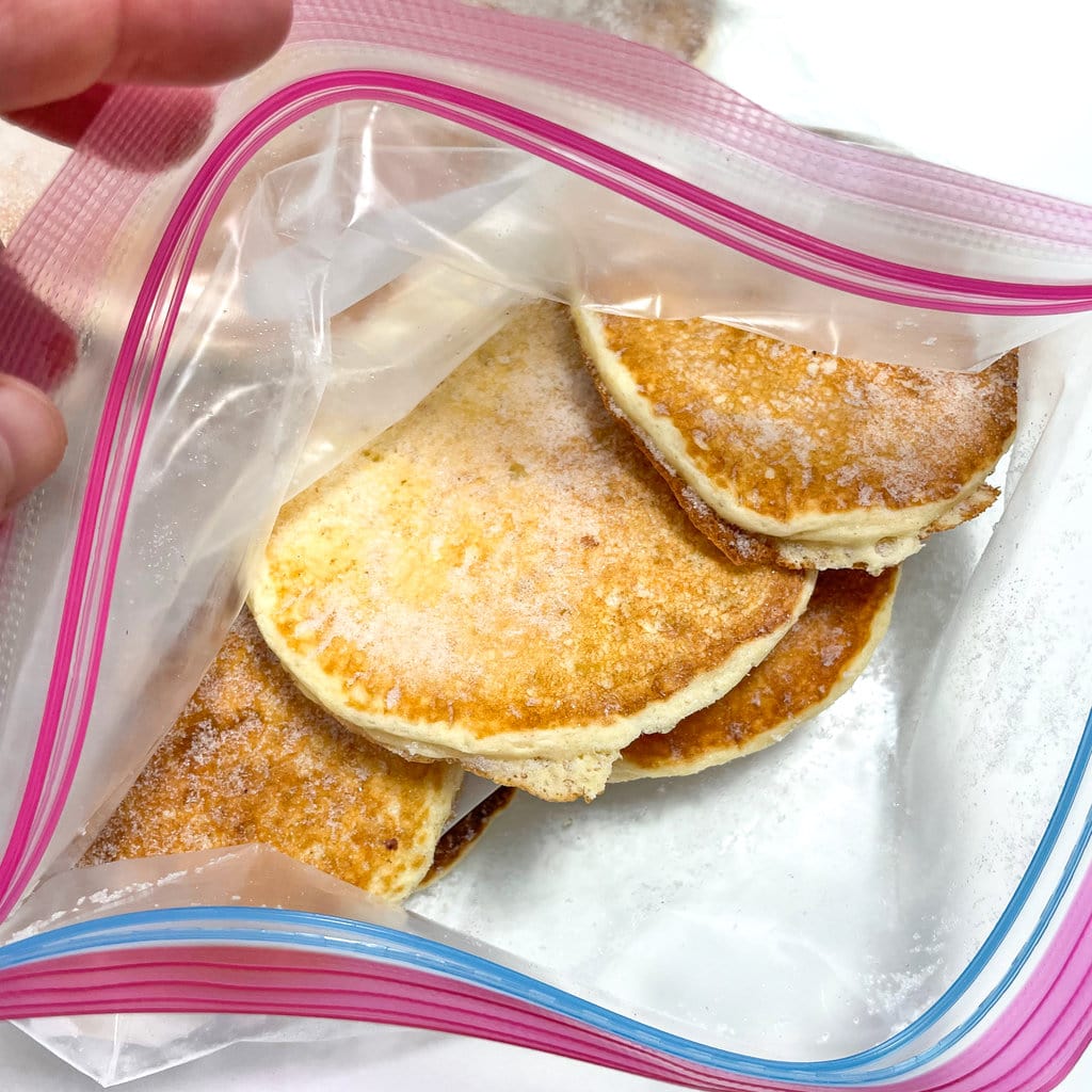 A hand lifting up a Ziploc bag showing frozen pancakes.