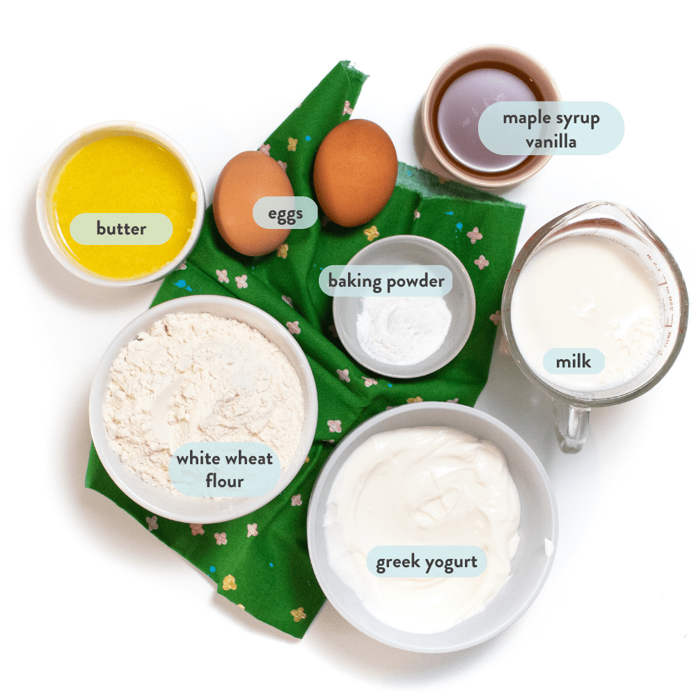 Spread of ingredients for yogurt muffins - yogurt, flour, baking powder, maple syrup, eggs and butter, on a green napkin on a white background