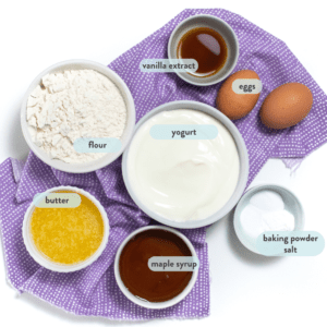 Ingredients for yogurt muffins spread on a purple napkin on a white background.