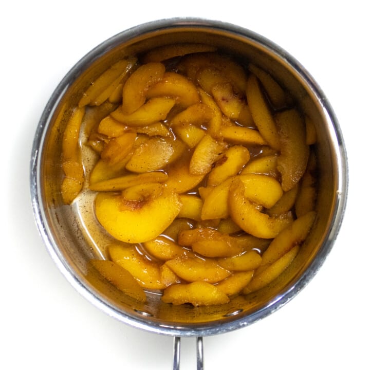 A silver saucepan with simmered peaches, maple syrup and vanilla.