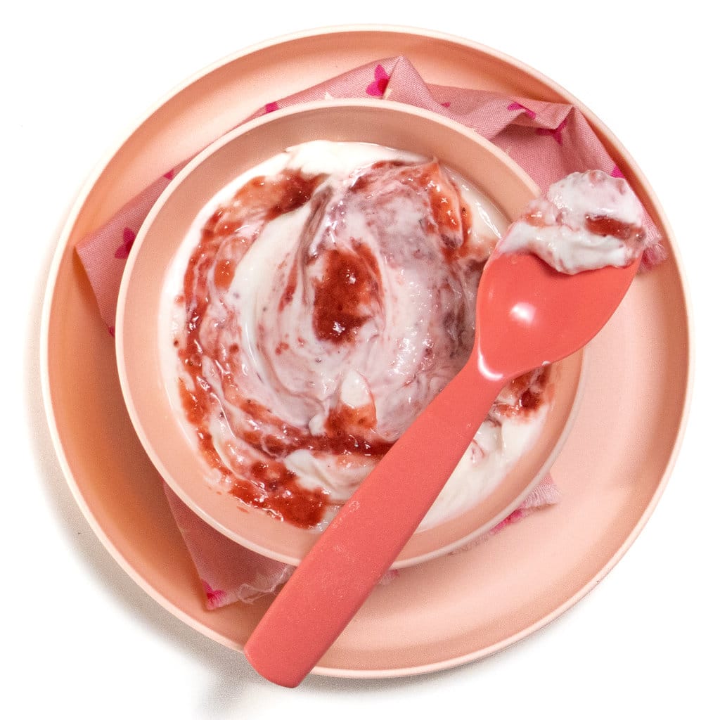 A pink bowl and plate filled with a white yogurt and strawberry purée swirled in against a white background.