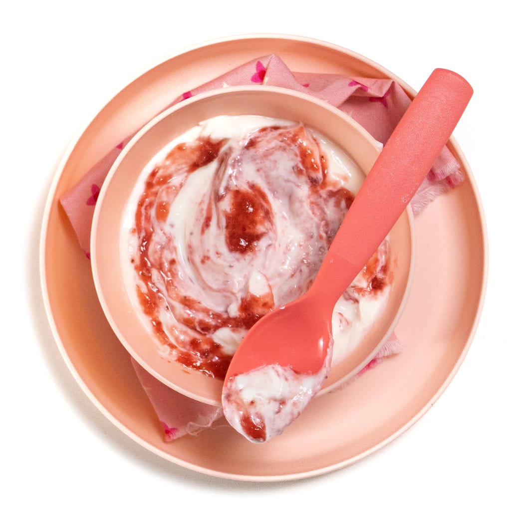 A pink kids bowl with a pink napkin and a pink spoon holding a strawberry yogurt for baby, toddler and kids.