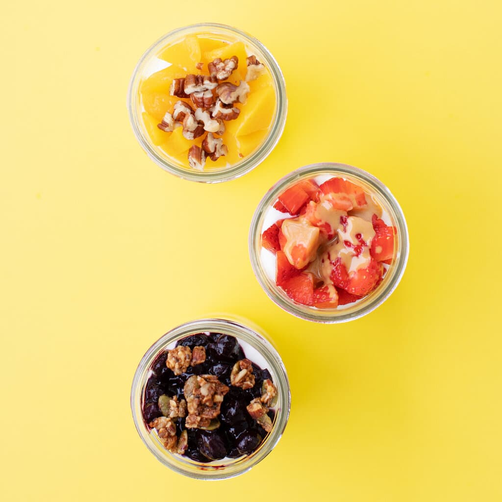 Three jars full of yogurt, fruit and toppings against the yellow background.