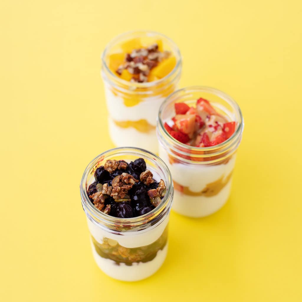 Three yogurt parfaits in a line full of fruits and other toppings.