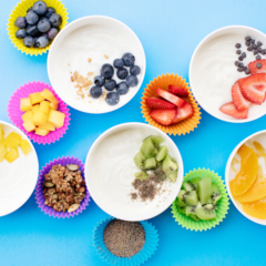 A spread of bowls full of yogurt with colorful small cups full of different toppings against a blue background.