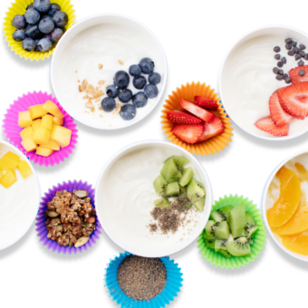 A spread of bowls full of yogurt with colorful small cups full of different toppings against a white background.