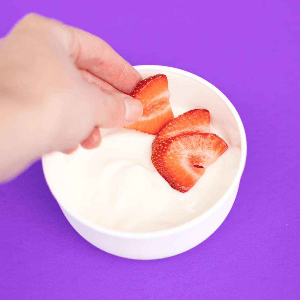 Putting strawberries in a bowl of yogurt.