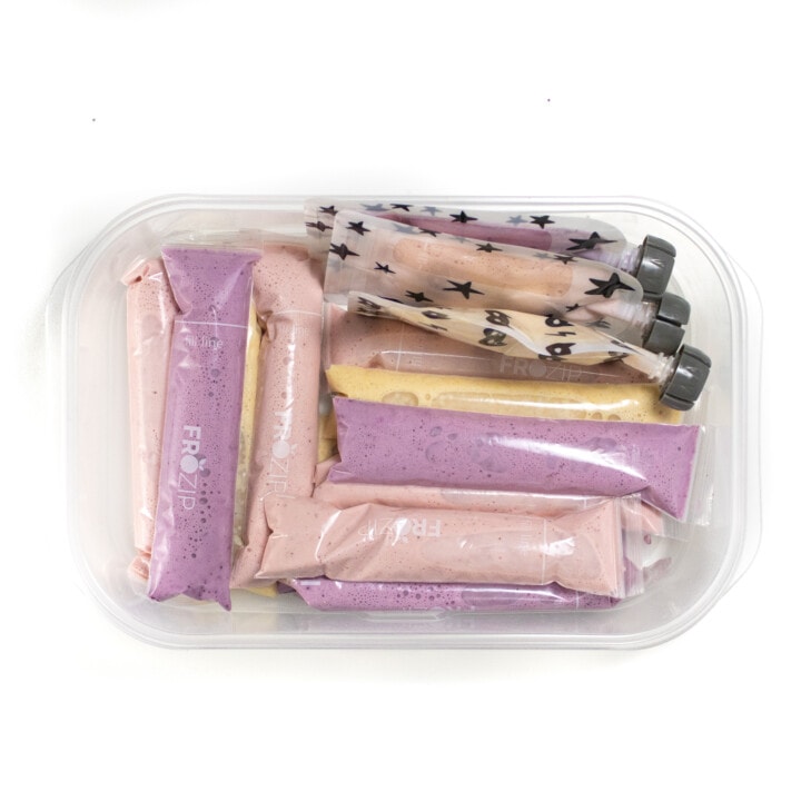 A white kitchen container filled with different yogurt tubes and pouches ready to be frozen.
