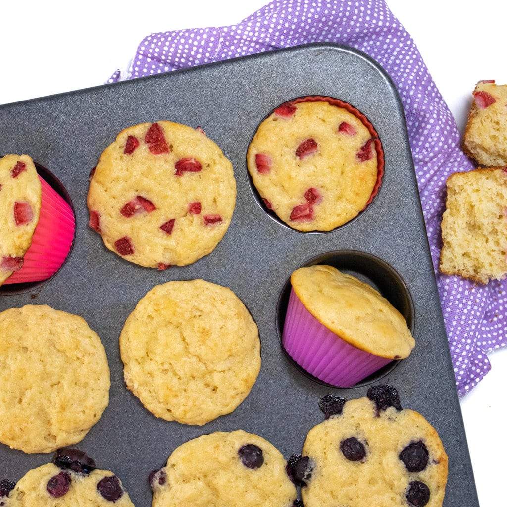 A muffin tin filled with yogurt muffins and colorful liners with a purple napkin.