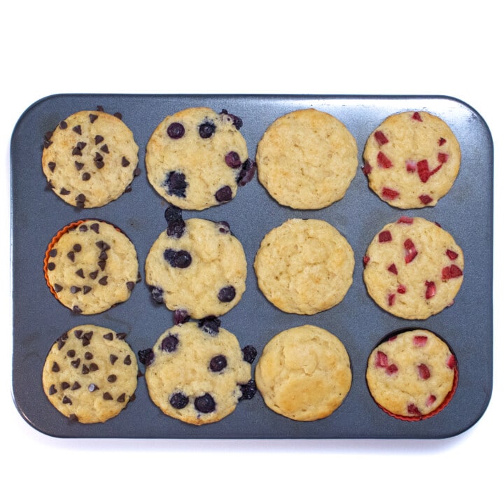 A muffin tin full of colorful liners, muffin batter and toppings.