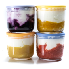 A side angle view of four different clear jars full with fruit on the bottom and yogurt on top with colorful lids.