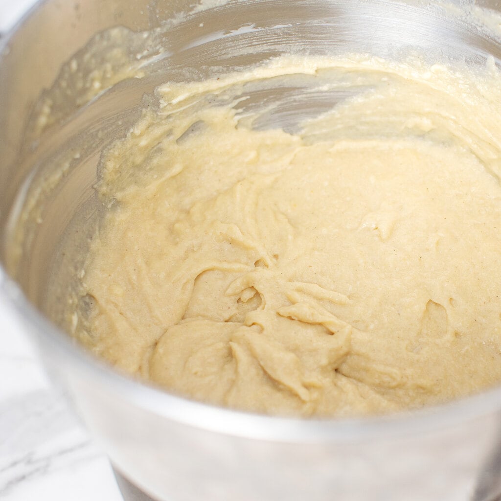 A bowl with a smash cake batter made with healthy ingredients such as applesauce, maple syrup, eggs, and milk.