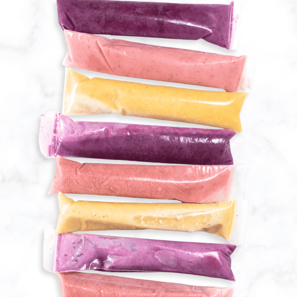 Row of homemade yogurt tubes on a marble counter. Tubes have three different flavors. 