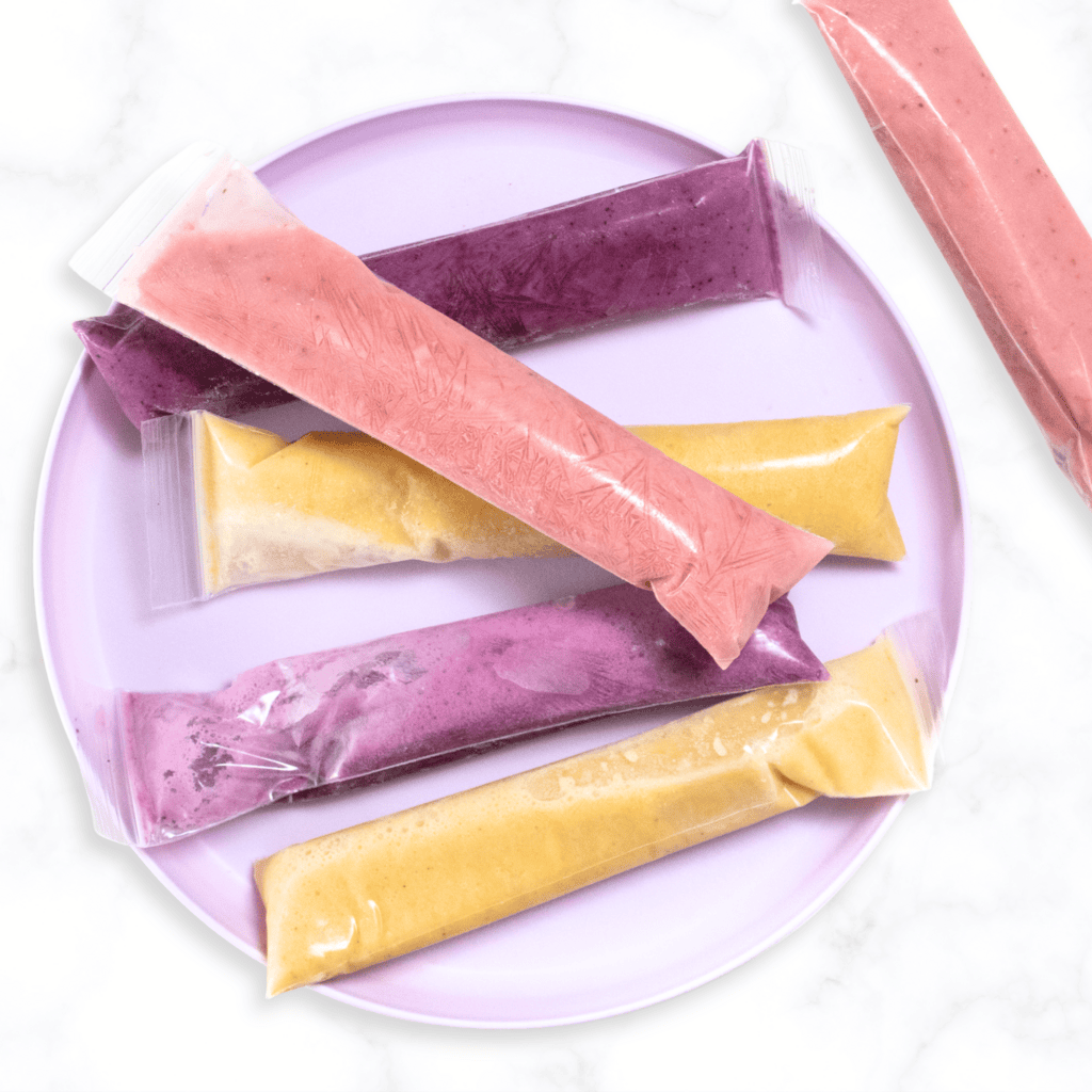 Purple kids plate sitting on a white marble counter with three different flavors of frozen yogurt tubes.