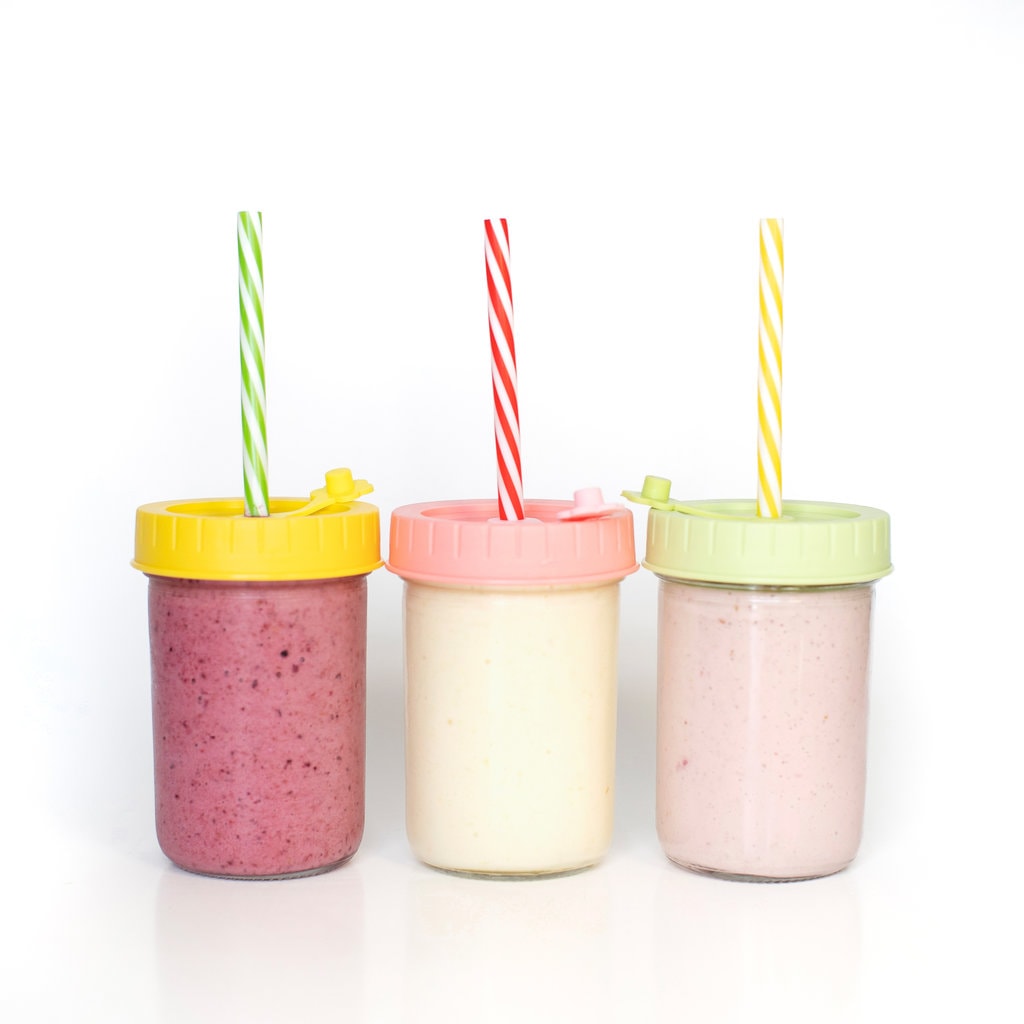 Is a view of three glass jars with colorful lids and straws for yogurt drinks for kids.