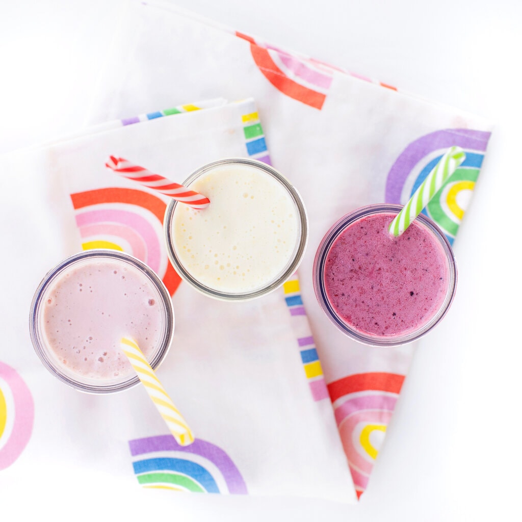 A rainbow napkin with three yogurt drinks with colorful striped straws coming out of them for kids.
