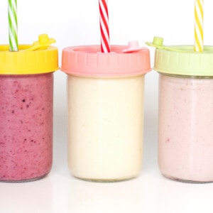 Is a view of three glass jars with colorful lids and straws for yogurt drinks for kids.