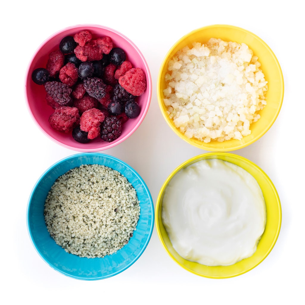 Four colorful kids bowls full of healthy ingredients for yogurt drinks.