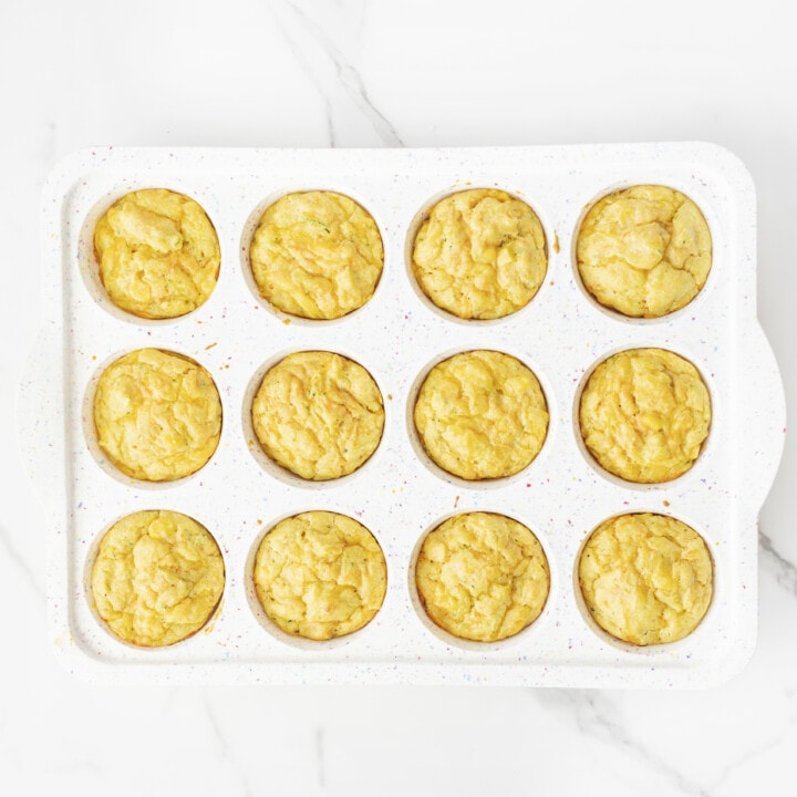 Cooked veggie muffins in a white muffin tin and get on a white marble backgrounds.