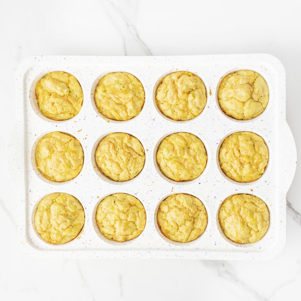 Cooked veggie muffins in a white muffin tin and get on a white marble backgrounds.
