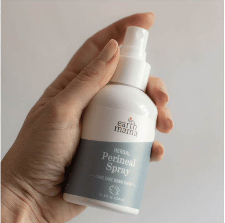 Hand holding a bottle of perineal spray that is white and blue. 