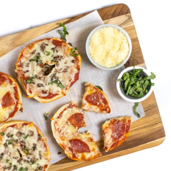 Cutting board with bagel pizzas Parmesan and basil cut into wedges.