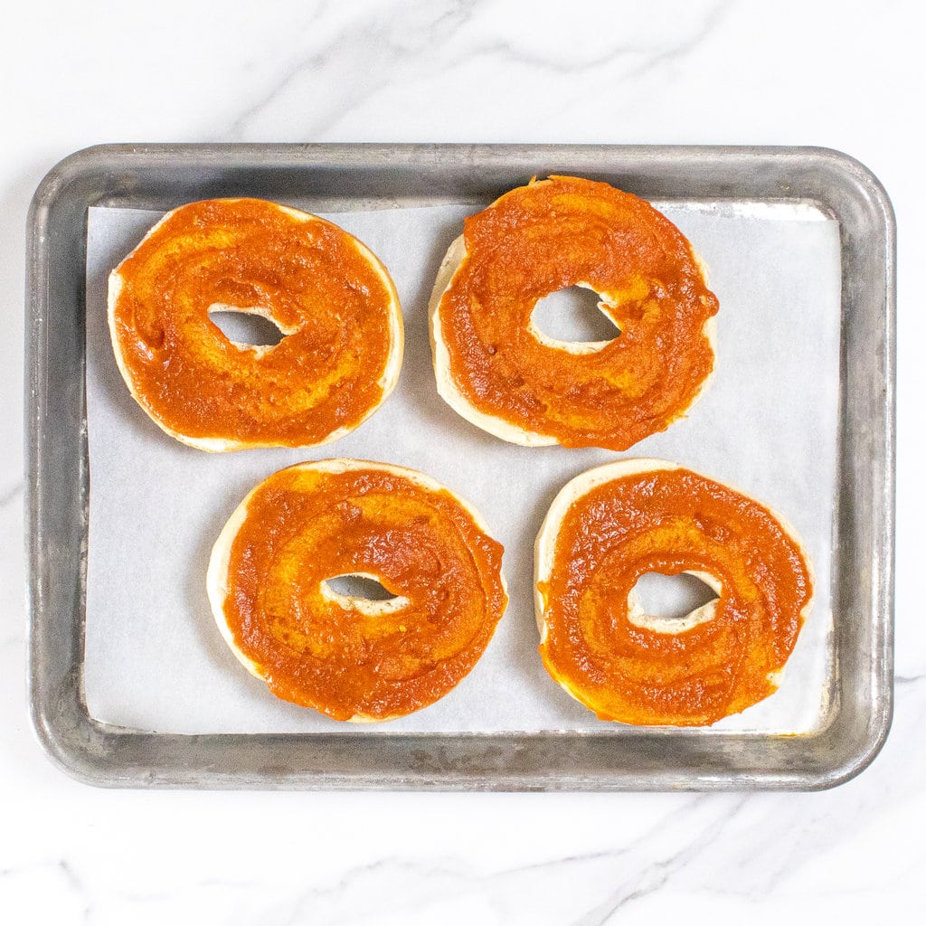 Bagels with hidden veggie tomato sauce on a baking sheet against a marble backdrop.