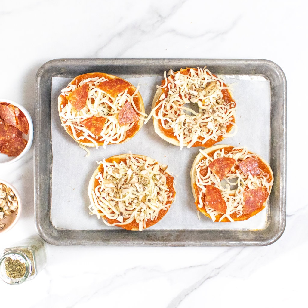 Showing how to load up a bagel pizza with different toppings.