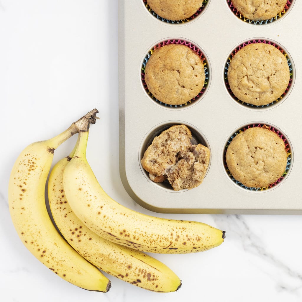 Baked banana muffins sitting on a marble counter with bananas sitting next to them.