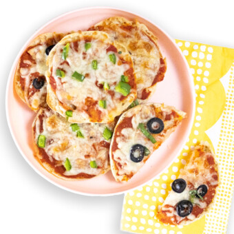 A pink kids play with English muffin pizzas on top in a yellow printed napkin.