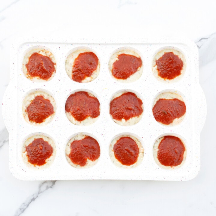 A white muffin tin full of pizza muffin batter ready to be baked.