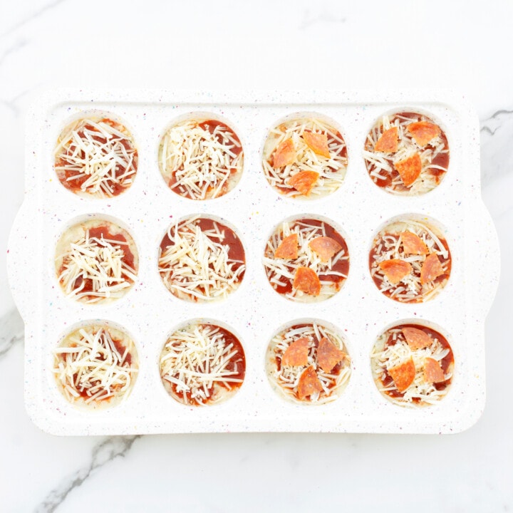 A white muffin tin full of pizza muffin batter ready to be baked.
