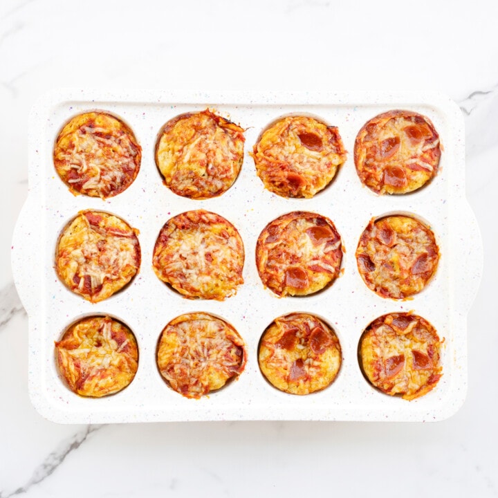 White muffin tin on a marble counter full of baked pizza muffins.