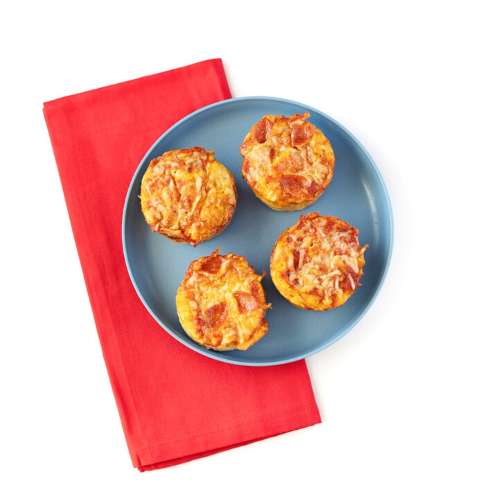 A gray kids plate with a red napkin on a white background. The plate has four pizza muffins on top.