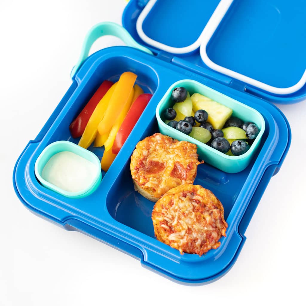 A blue lunchbox full of pizza muffins, blueberry and pineapple, pepper sticks and ranch.