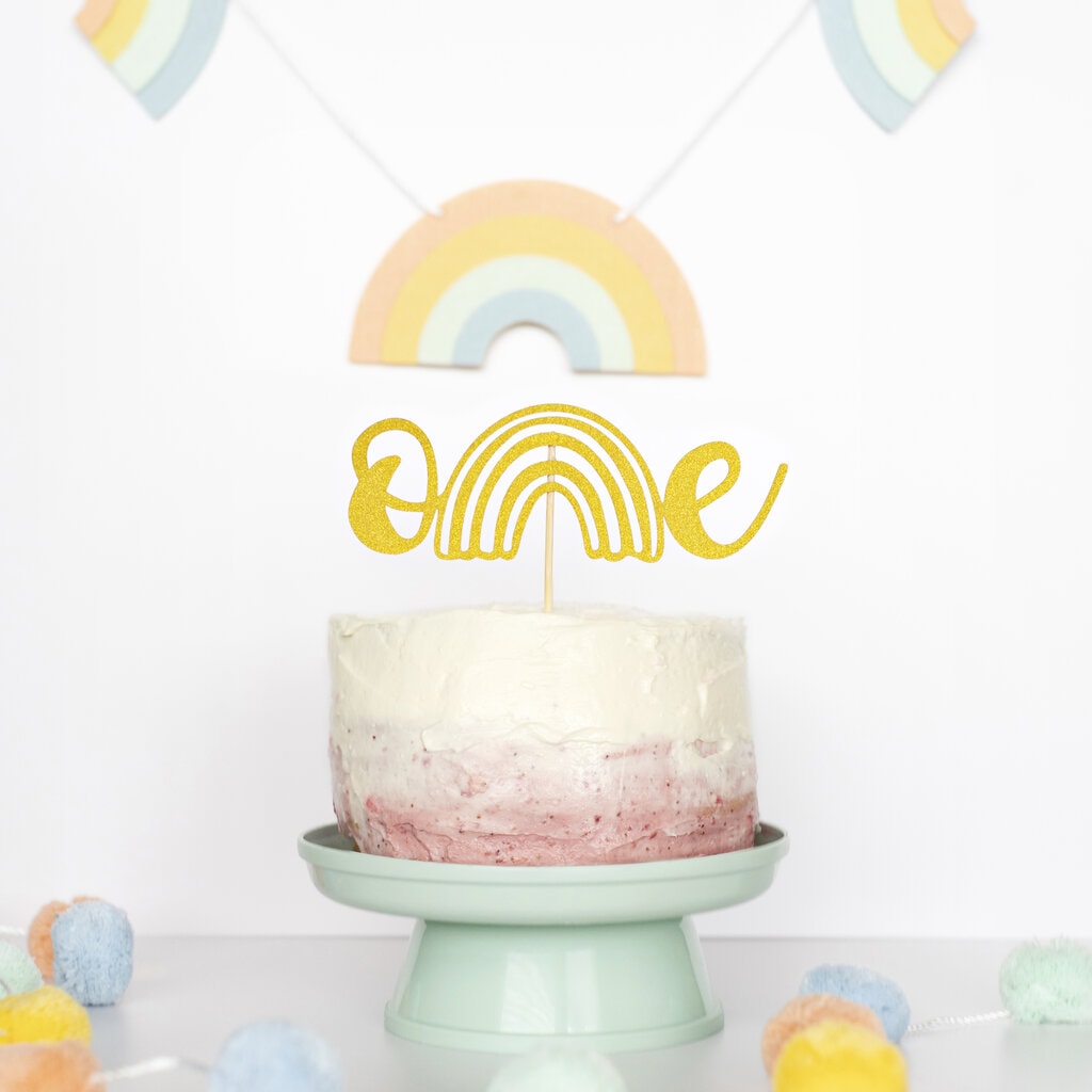 Smash cake with pink and white frosting on a teal cake stand with a slice of cake next to it on a blue plate.