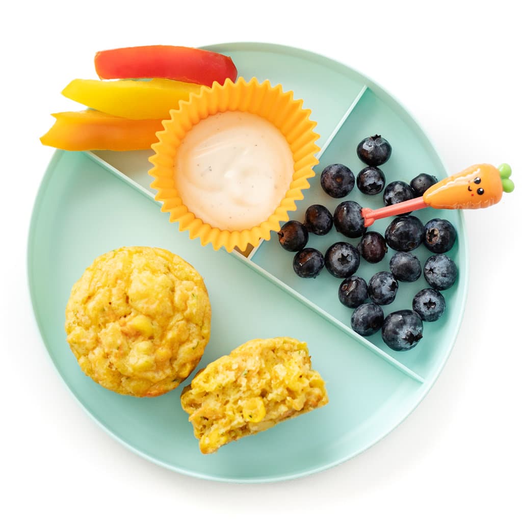 A sections blue plate for kids with veggie muffins, blueberries, veggie sticks and ranch dip against a white background.
